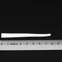 Biały pasek papieru, który może posłużyć do zmierzenia rozmiaru pierścionka 11, leży nad linijką.