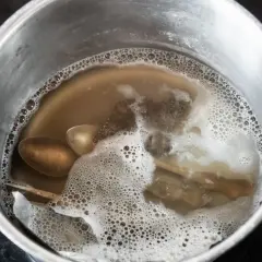 Srebrne łyżki i folia aluminiowa w garnku z bulgoczącą wodą.