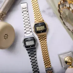 Dwa zegarki Casio, srebrny i złoty, obok retro telefonu. Idealne dla kobiet ceniących styl, często pojawiają się w rankingach luksusowe zegarki damskie ranking.