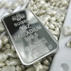 Sztabka palladu 1 uncja 999,5 na tle luźnych granulek tego cennego metalu.