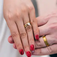 Dłonie pary z obrączkami. Na palcu kobiety pierścionek z brylantem, na palcu mężczyzny prosta obrączka. Oba wykonane z najniższa próba złota.