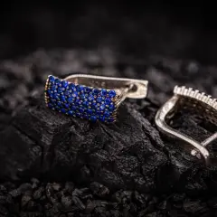 Eleganckie kolczyki z niebieskimi kamieniami, zapięcie angielskie, prezentowane na tle węgla drzewnego.