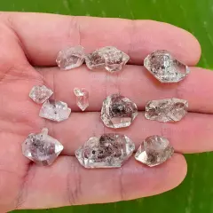 Dłoń trzyma kilka surowych kryształów diamentu Herkimer. Kamienie są przezroczyste, z widocznymi inkluzjami.