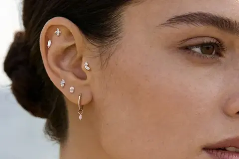 Ucho ozdobione wieloma błyszczącymi kolczykami, od krzyżyka po wiszące krople. Migracja kolczyka w górę ucha dodaje stylizacji uroku.