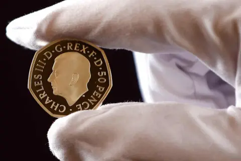 Złoty suweren moneta z wizerunkiem Karola III, trzymana w białej rękawiczce.