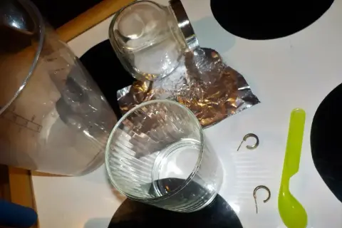 Przygotowania do czyszczenia złota folią aluminiową: szklanki, słoik, folia, łyżeczka i kolczyki.