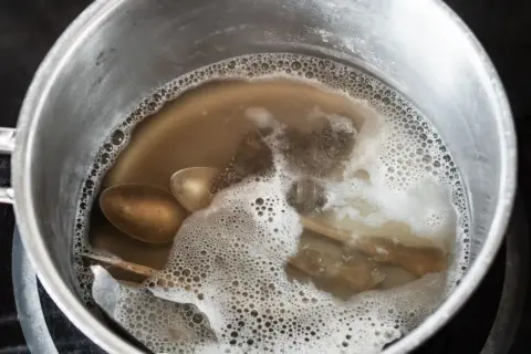 Srebrne łyżki i folia aluminiowa w garnku z bulgoczącą wodą.