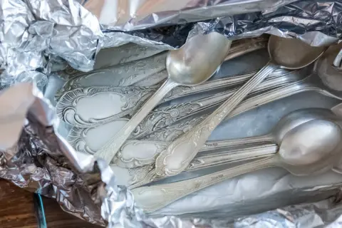 Stos srebrnych łyżek i widelców owiniętych w folię aluminiową.