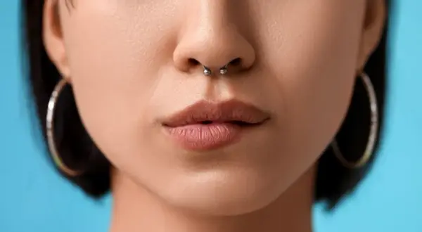 Zbliżenie na usta i nos z kolczykiem w septum. Delikatne, naturalne usta i srebrny kolczyk w przegrodzie nosowej.