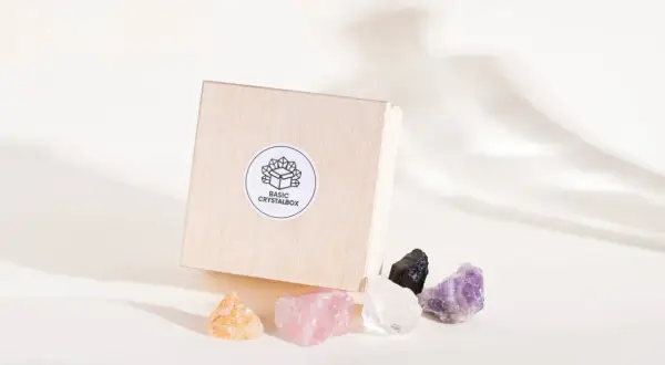 Drewniane pudełko z naklejką "BASIC CRYSTALBOX" i pięcioma surowymi kamieniami: bursztynowym, różowym kwarcem, kryształem górskim, czarnym turmalinem i ametystem. Każdy cenny kamień emanuje naturalnym blaskiem.