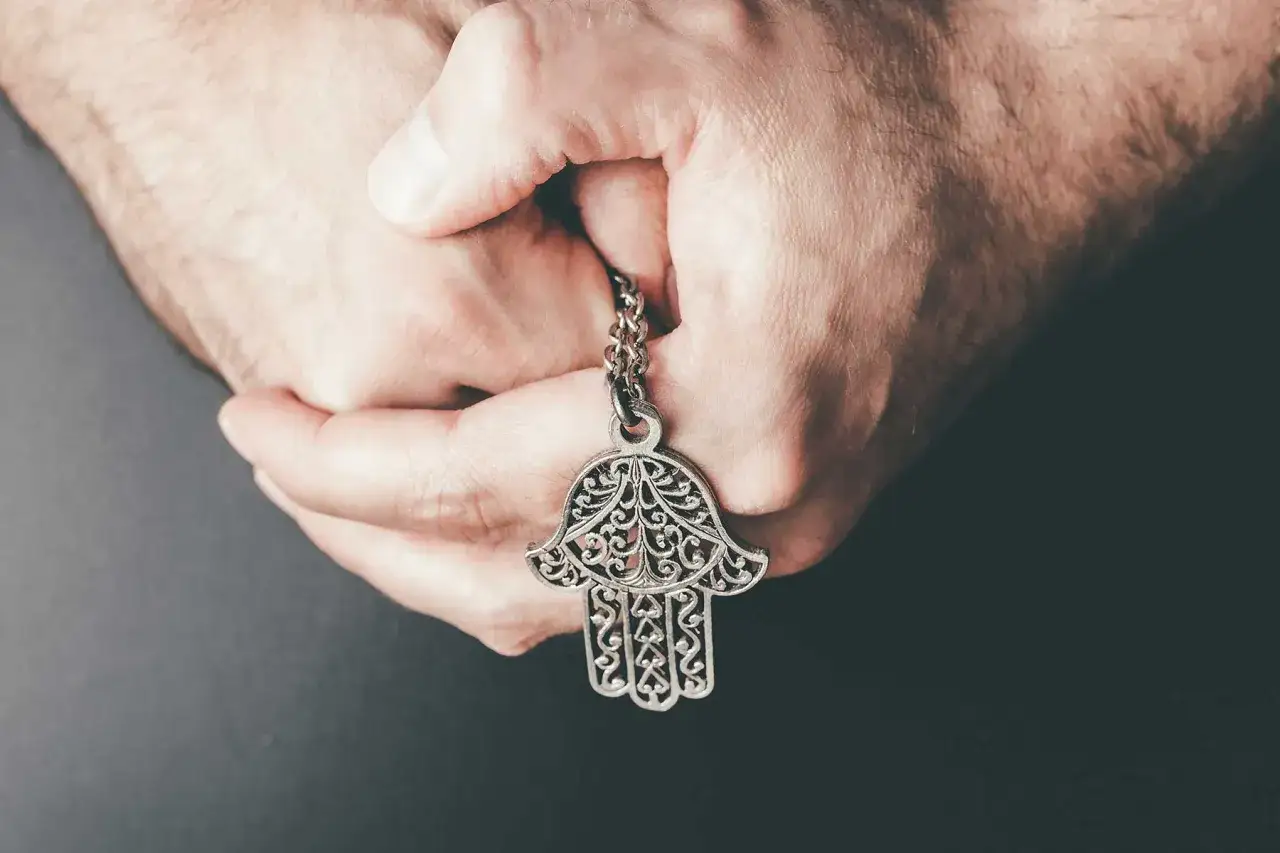 Dłonie trzymają ozdobny wisiorek ręka fatimy.