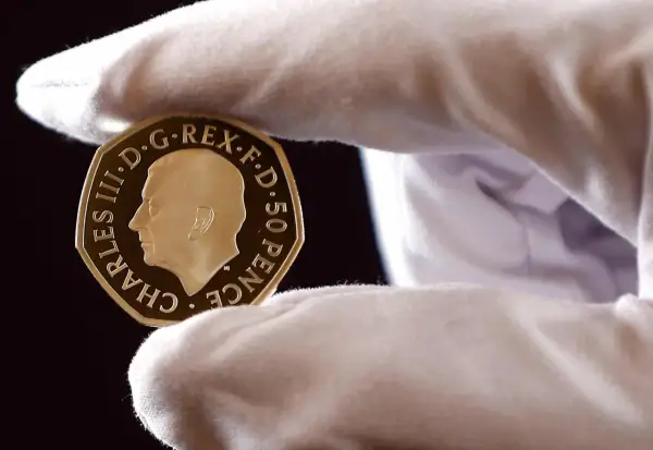 Złoty suweren moneta z wizerunkiem Karola III, trzymana w białej rękawiczce.