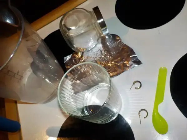 Przygotowania do czyszczenia złota folią aluminiową: szklanki, słoik, folia, łyżeczka i kolczyki.