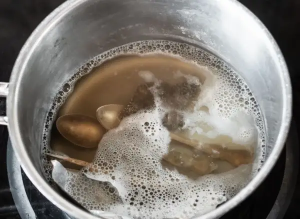 Srebrne łyżki i folia aluminiowa w garnku z bulgoczącą wodą.