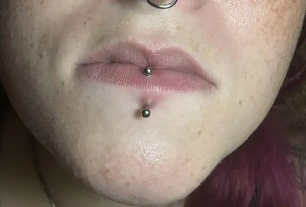 Labret co to? Kolczyk w wardze i pod nią, ozdobiony metalowymi kulkami. Skóra z piegami.