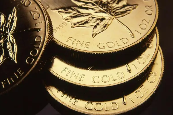 Stosik błyszczących monet ze złota inwestycyjnego z liściem klonu. Napisy "FINE GOLD" i "1 OZ" są wyraźnie widoczne.