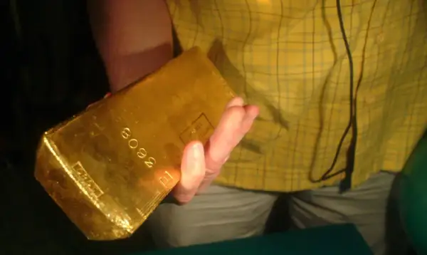 Dłoń trzyma błyszczącą sztabkę złota 5kg z wybitym numerem seryjnym.