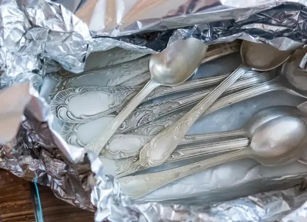 Stos srebrnych łyżek i widelców owiniętych w folię aluminiową.